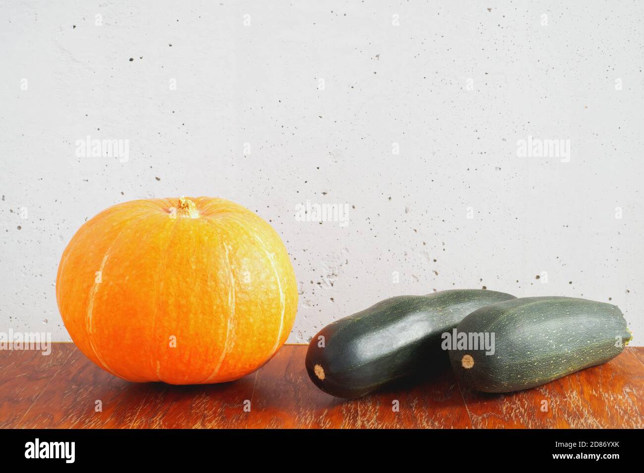 Orange pumpkin and two dark green zucchini on wooden table on gray concrete wall background. Copy space Stock Photo