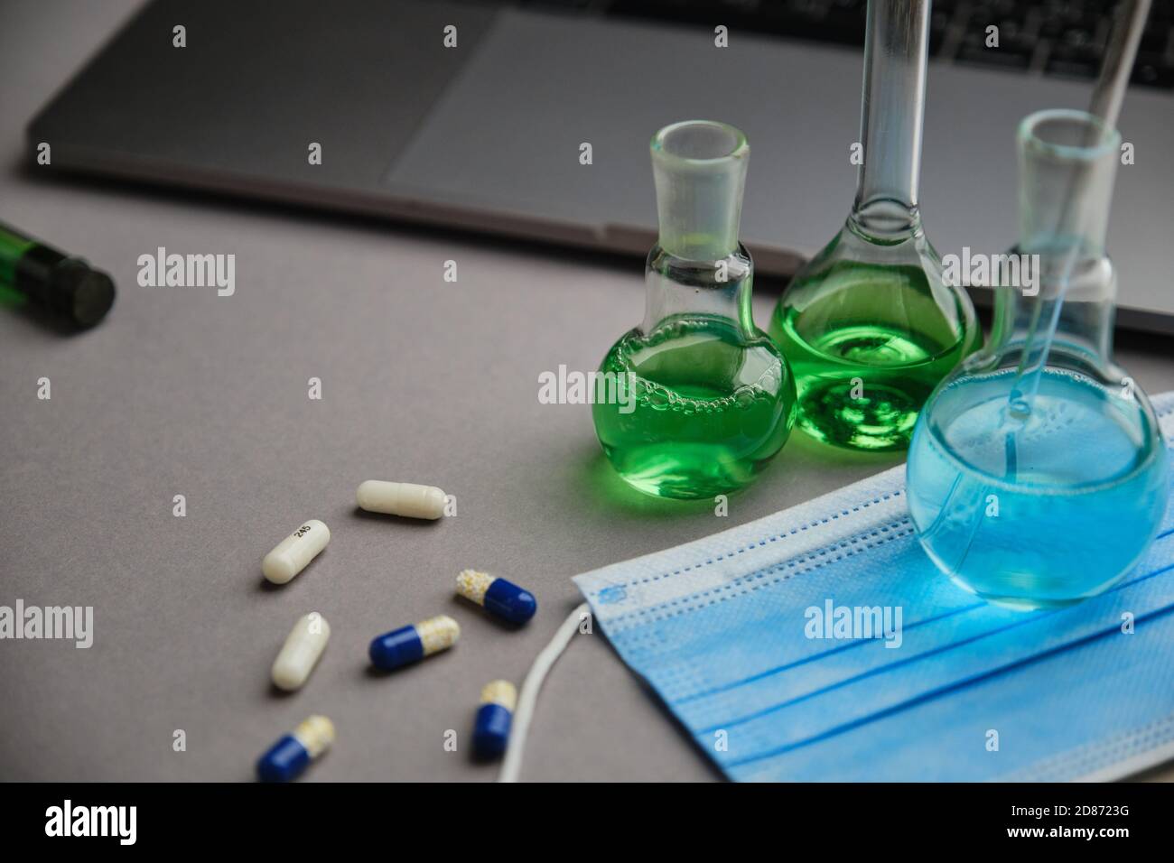 Laboratory flask with green and blue liquid and pills. Research for the virus cure and laptop Stock Photo