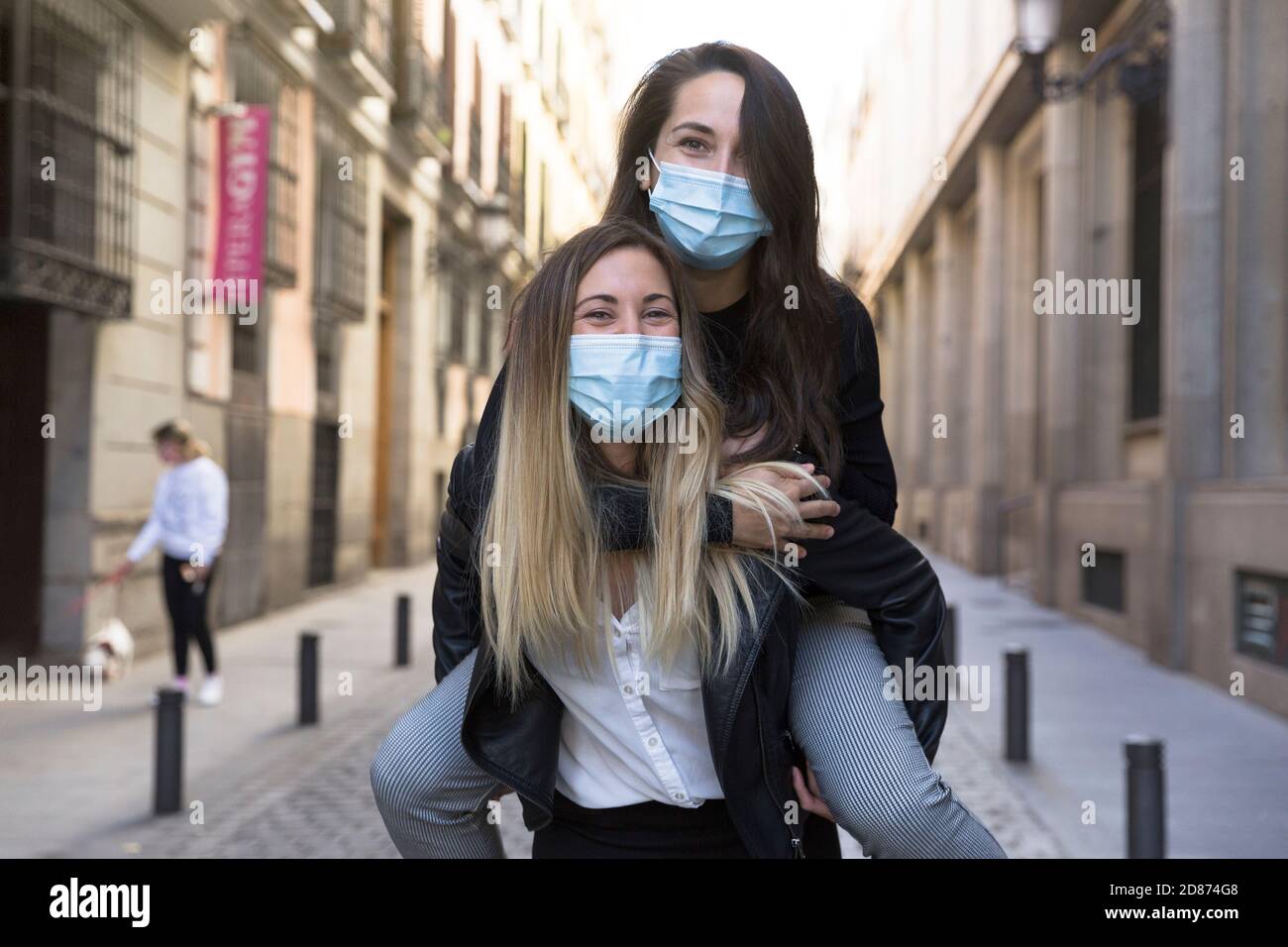 Two girls having fun on the street. They are wearing medical masks ...