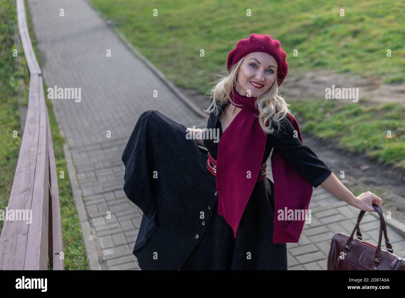 a girl walks up the stairs and in a burgundy palette and biret, an adult smiles at the camera in black clothes, in the fall against a background of Stock Photo