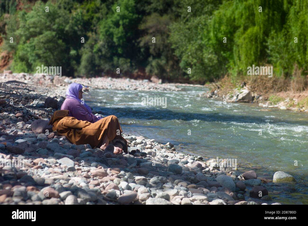 Moroccan couple with djellaba and headscarf sits and talk in on the bank at a river in Setti Fatma, Ourika Valley near Marrakech Stock Photo
