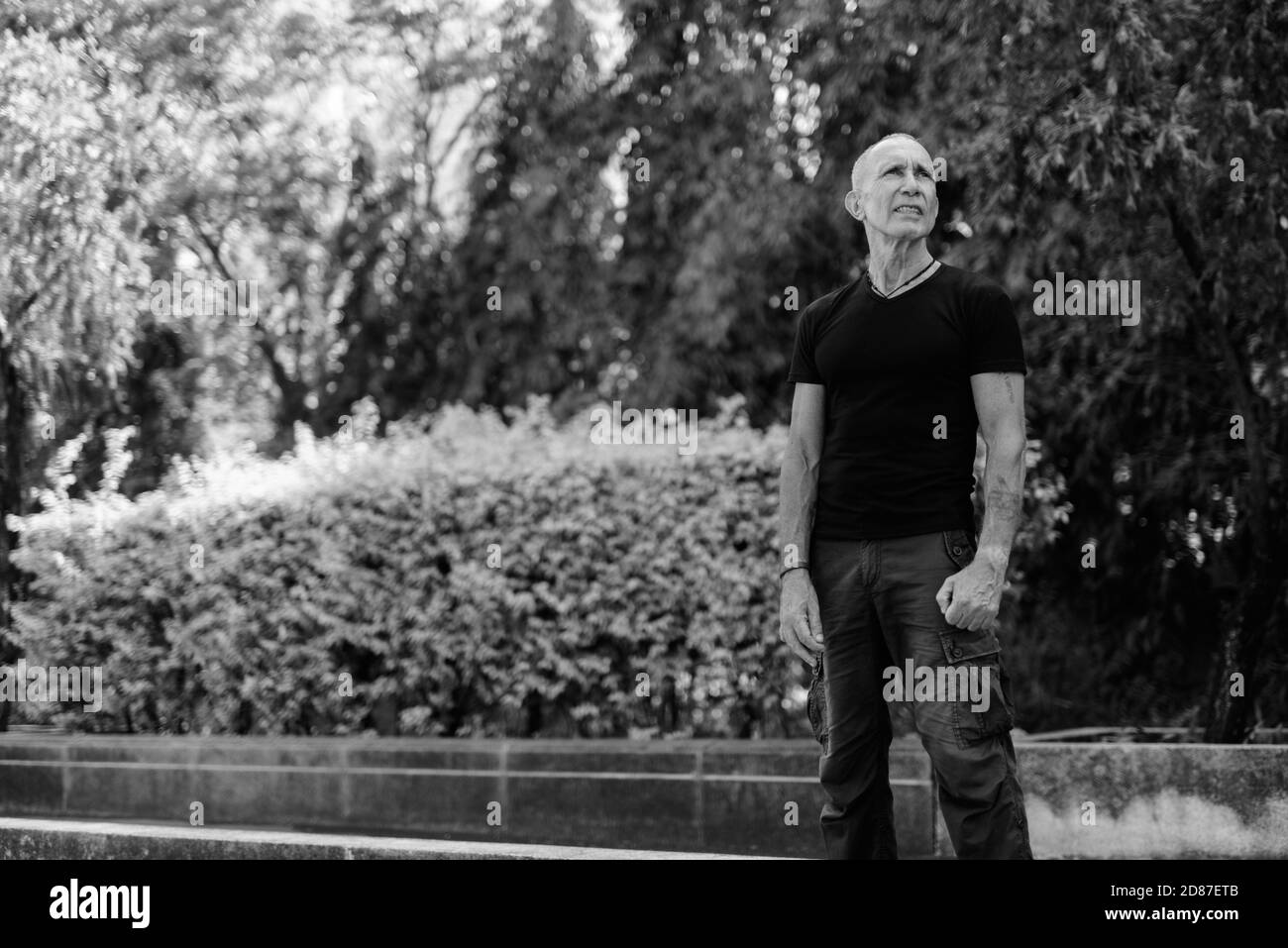 Bald senior tourist man standing and thinking while looking up at peaceful park in Bangkok Thailand Stock Photo