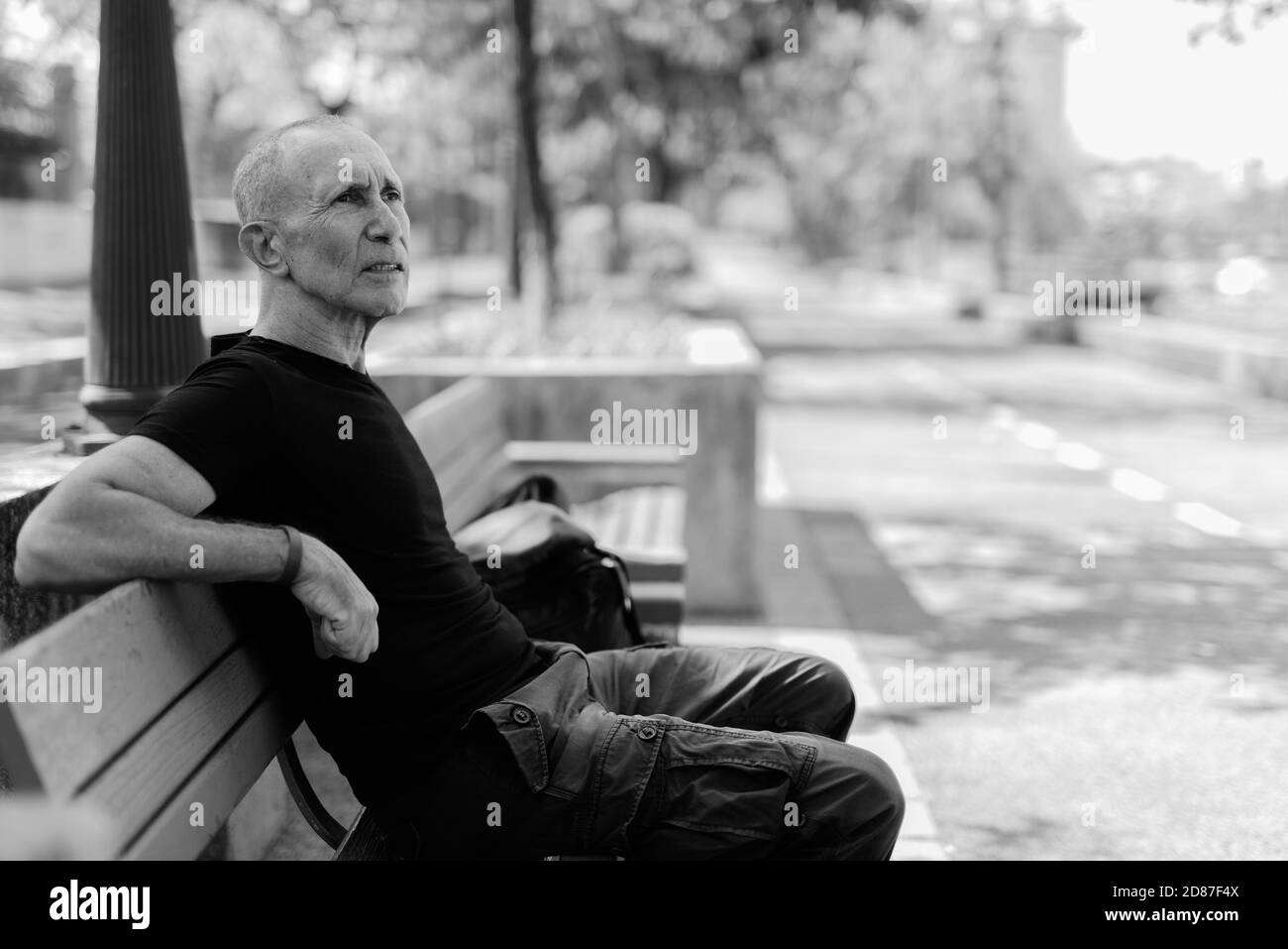 Bald senior tourist man thinking while sitting on the wooden bench at peaceful park in Bangkok Thailand Stock Photo
