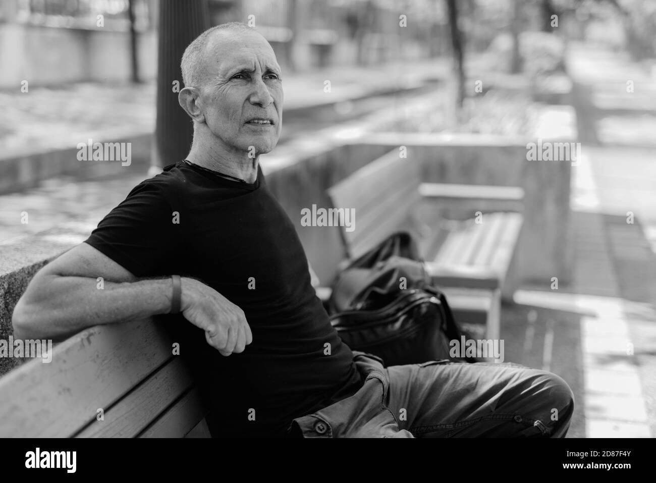 Bald senior tourist man thinking on the wooden bench at peaceful park in Bangkok Thailand Stock Photo