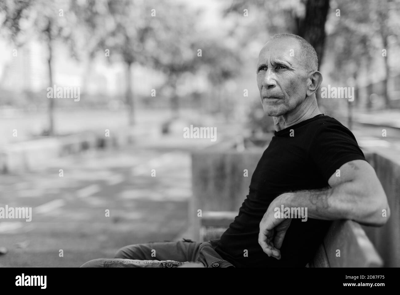 Bald senior tourist man with hand tattoos thinking and sitting on the wooden bench at peaceful park in Bangkok Thailand Stock Photo