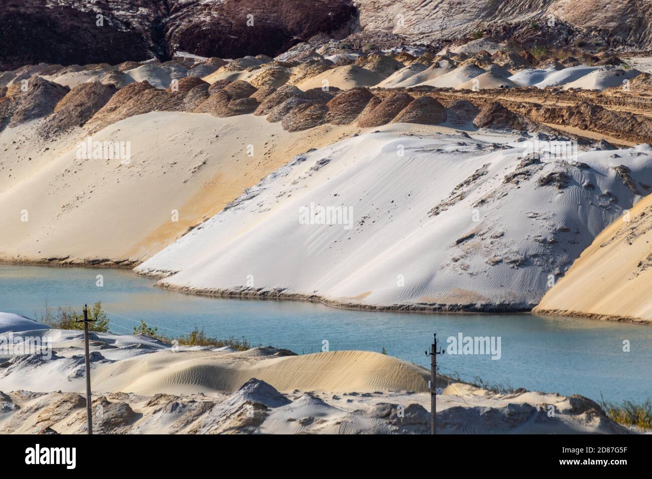 White and yellow sand dunes hills near blue lake water terrain. Landscape of sand extraction at quarry Stock Photo