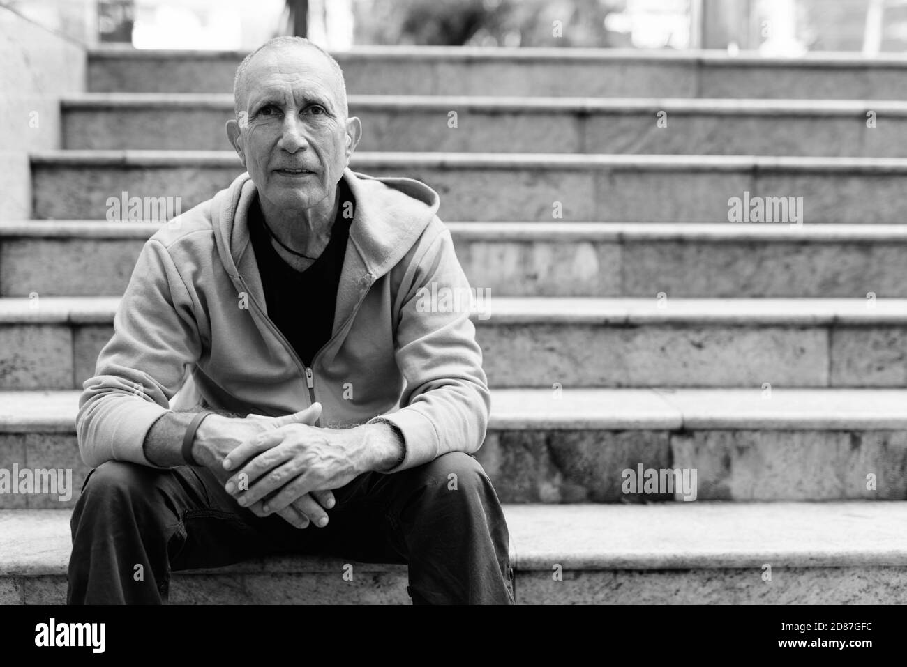 Bald senior man leaning arms on knees while sitting on the staircase in Bangkok Thailand Stock Photo