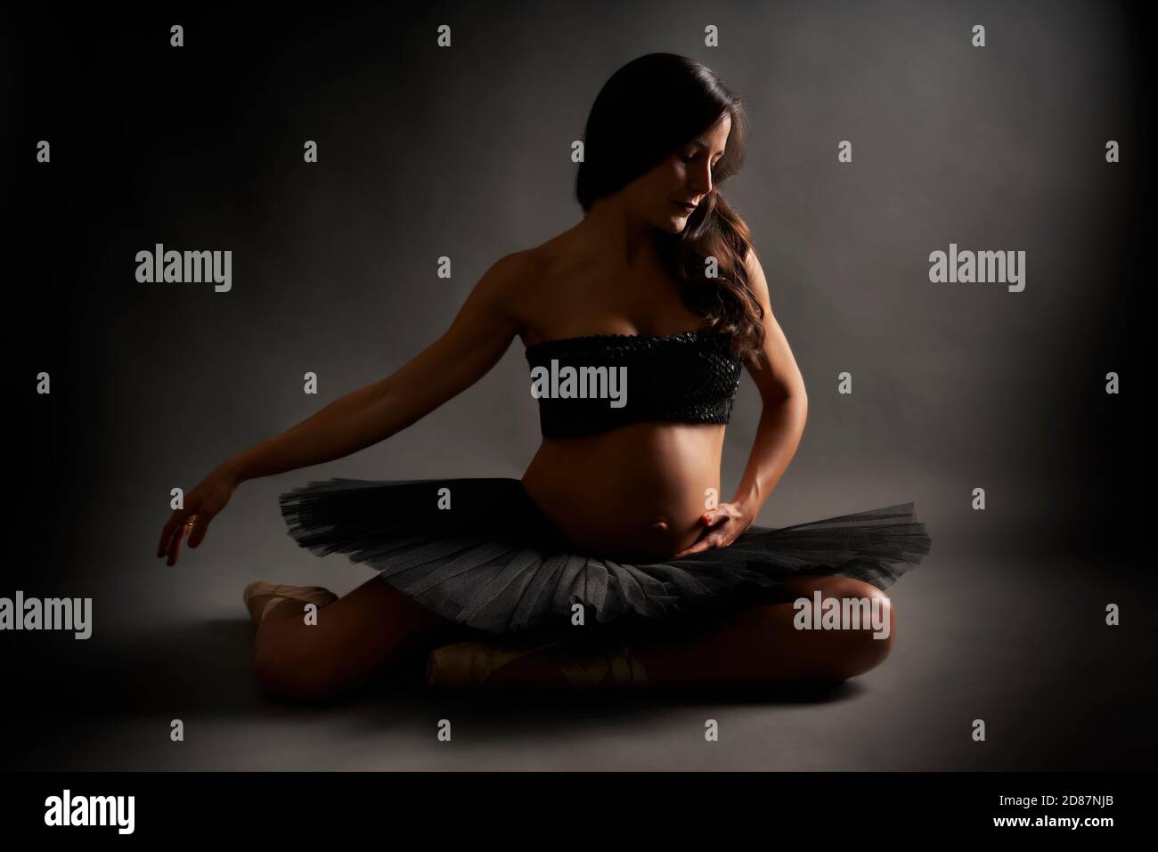 Young pregnant ballerina performing classical ballet pose with black top and tutu in studio Stock Photo