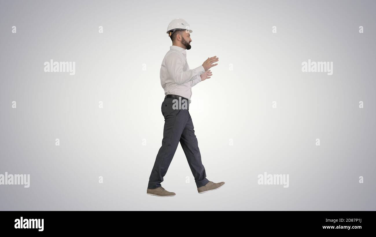 Engineer in hardhat walking and explaining something on gradient Stock Photo