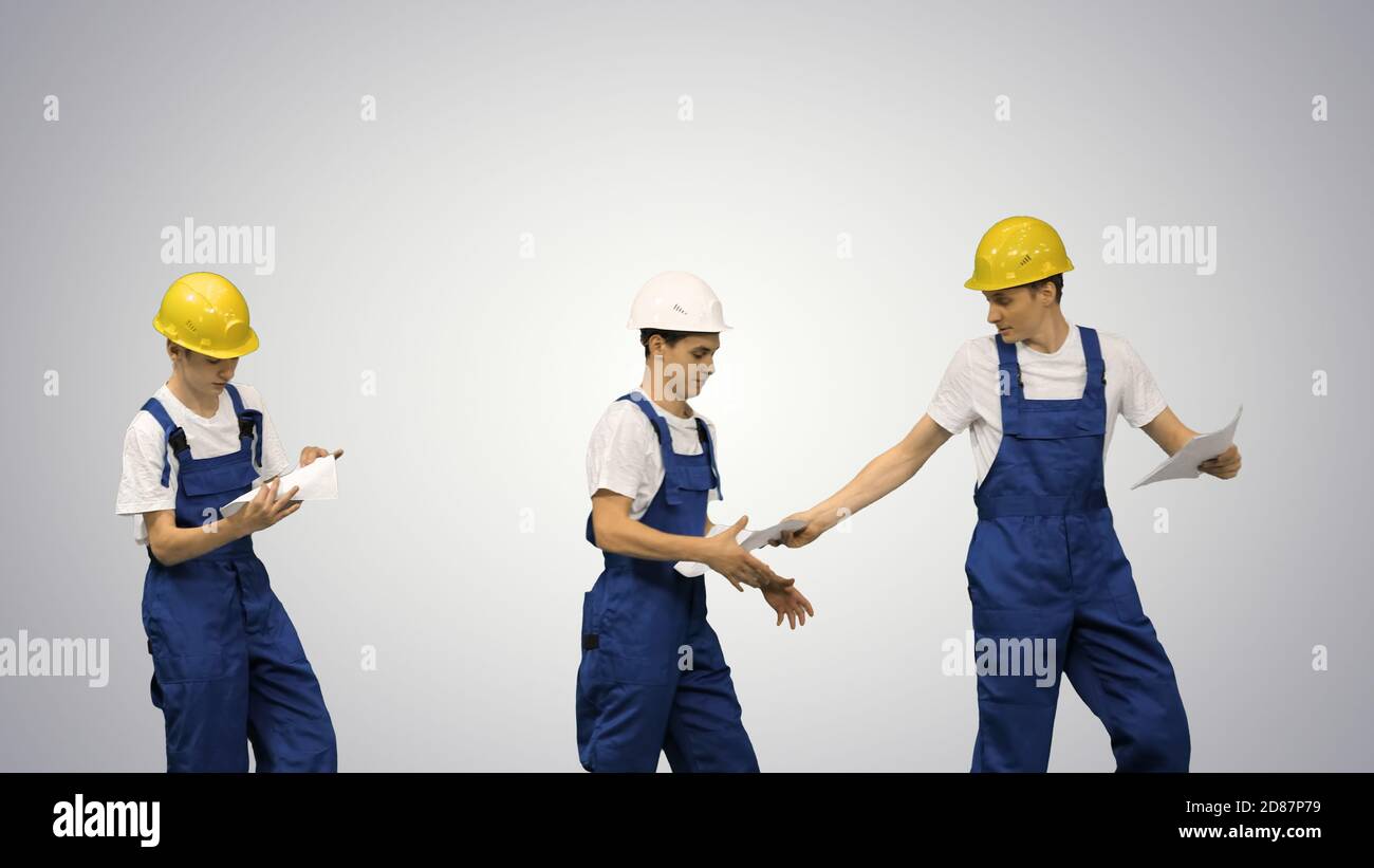 Three young construction workers in hardhats passing on document Stock Photo