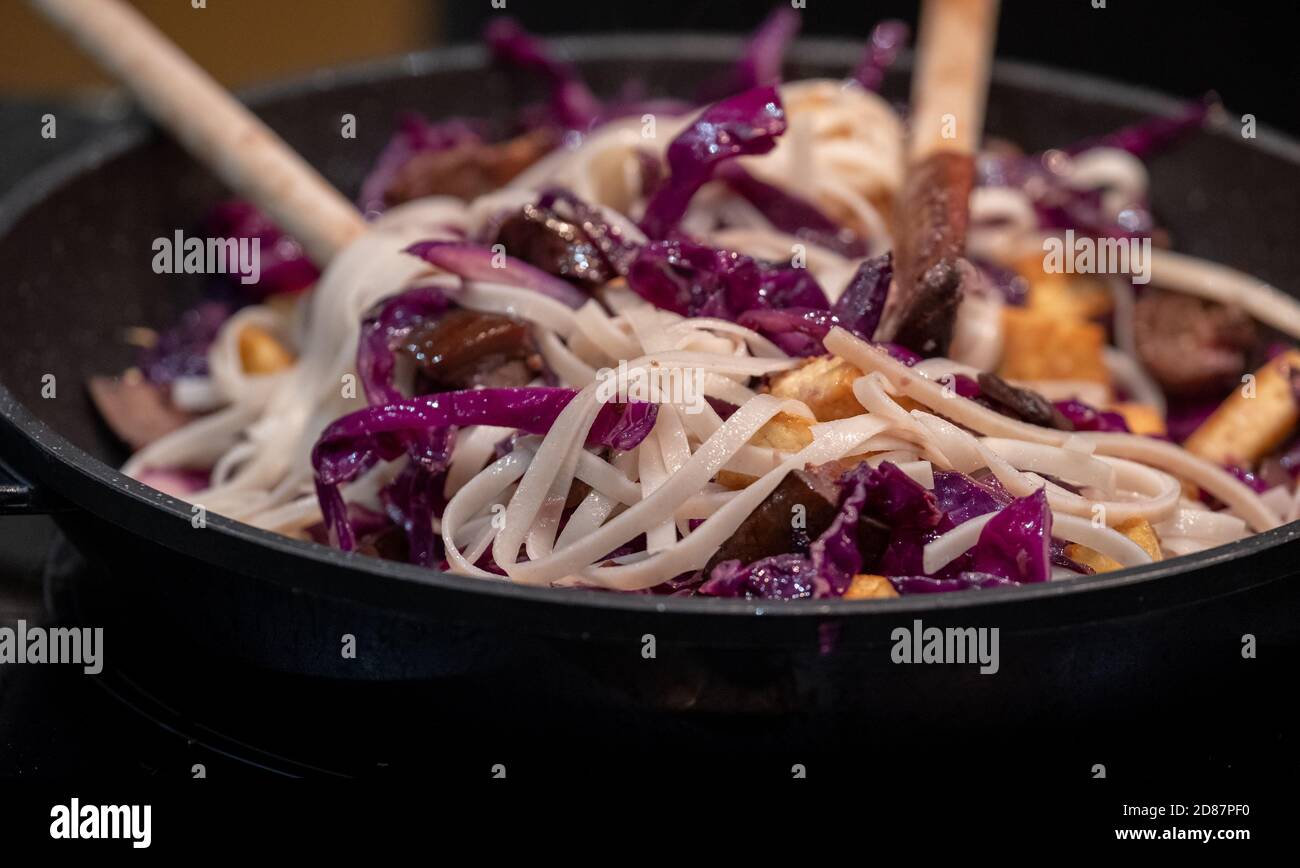 Preparing a vegan Asian Pad Thai stir fry with red cabbage, tofu, aubergine and noodles. Stock Photo