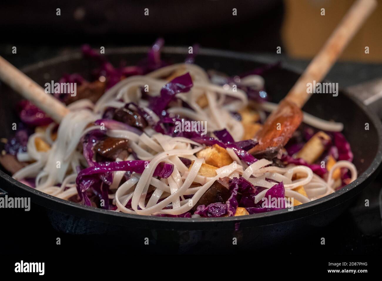 Preparing a vegan Asian Pad Thai stir fry with red cabbage, tofu, aubergine and noodles. Stock Photo