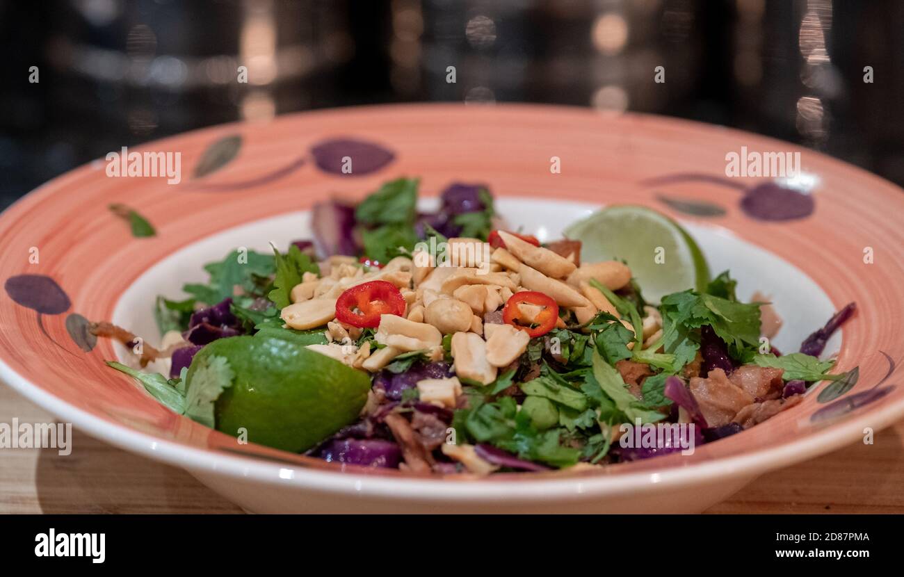 Bowl of vegan Asian style Pad Thai stir fry with red cabbage, aubergine, tofu and noodles. Garnished with peanuts, lime and red chilli pepper. Stock Photo