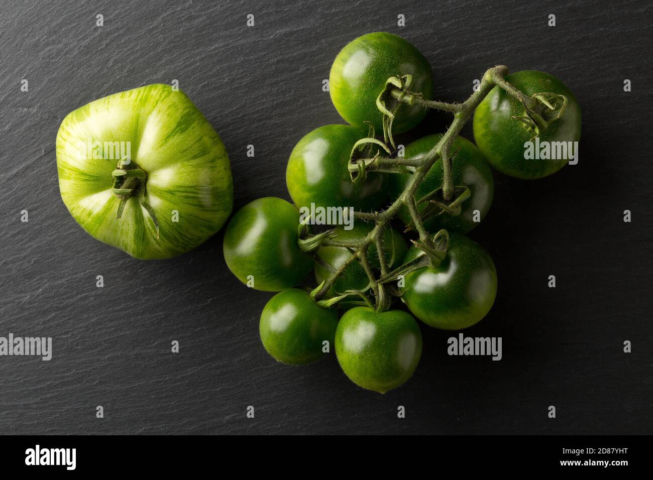 Unripe green tomatoes on dark stone plate background, unripe tomatoes can be fried or used for relish, selective focus, flat lay top view from above Stock Photo