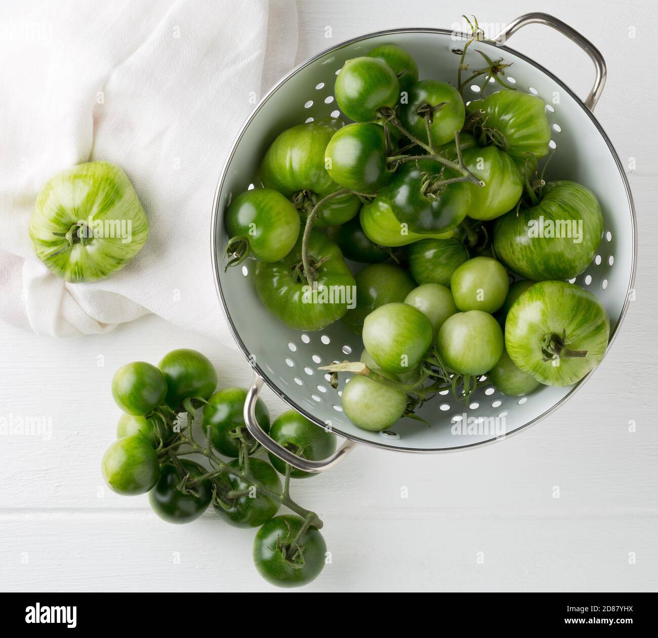 Unripe green tomatoes in colander and on table in white wooden kitchen background, unripe tomatoes can be fried or used for relish, selective focus, f Stock Photo