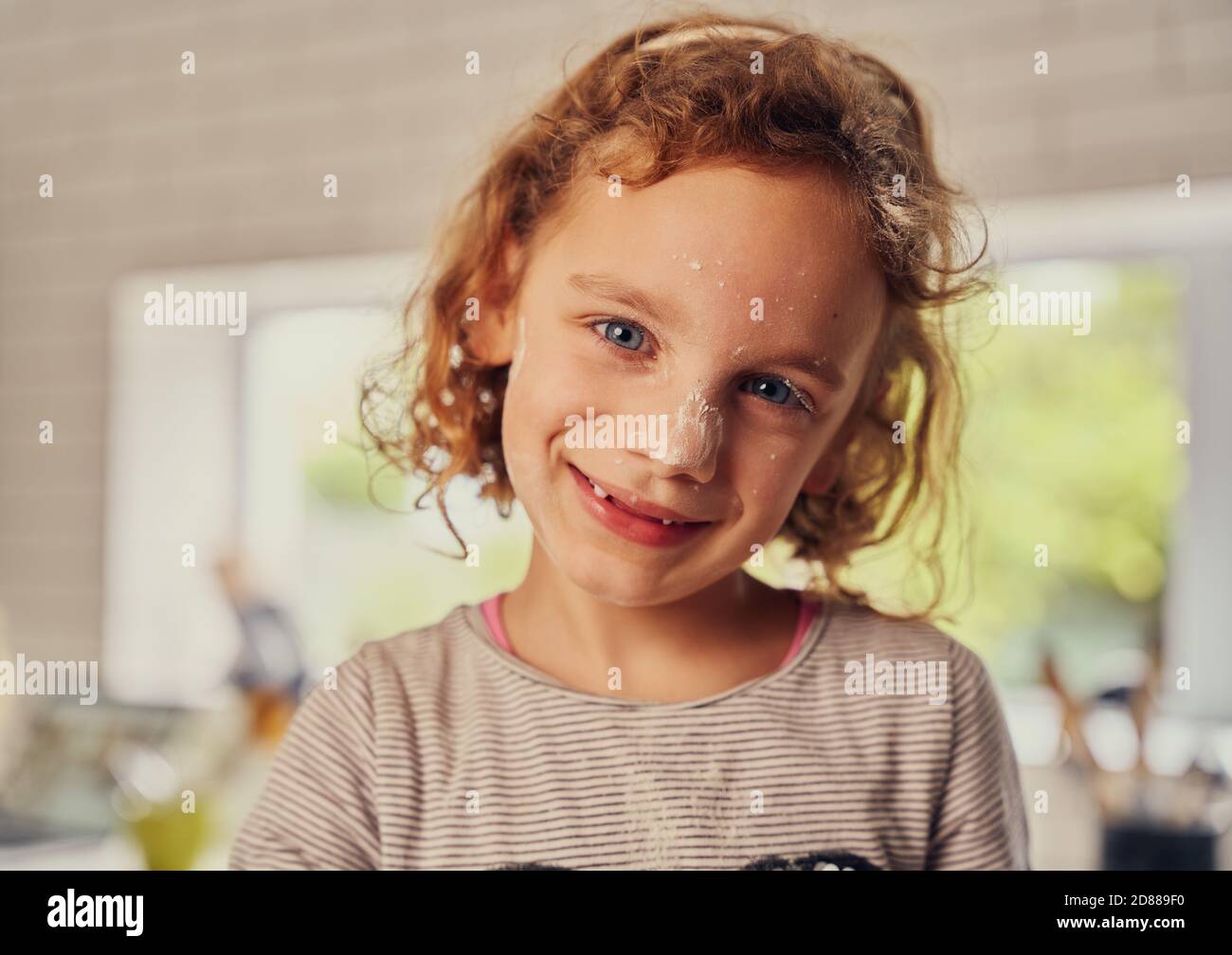 Portrait of cheerful little girl cooking in kitchen with flour applied ...