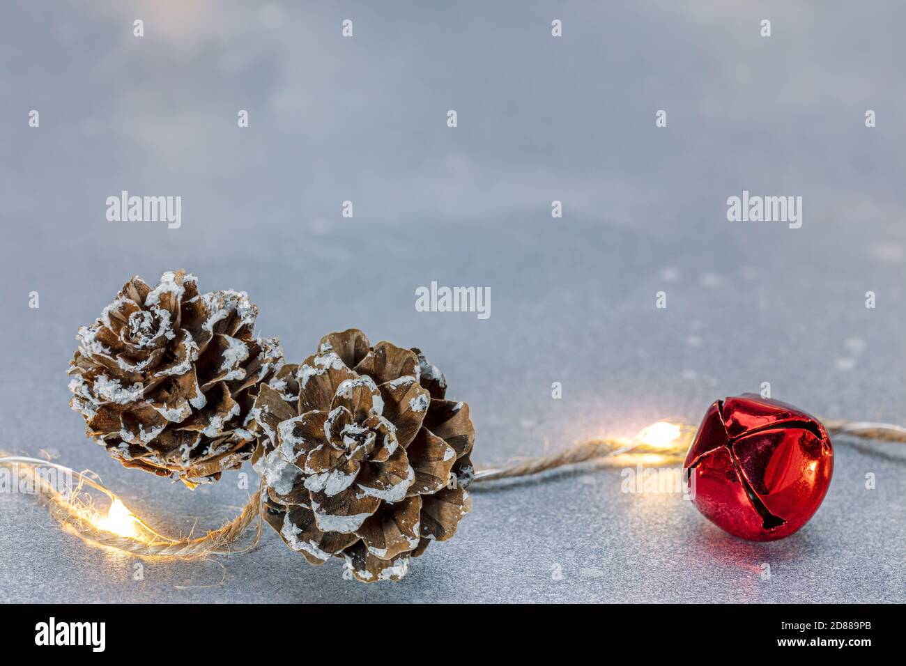 new year decorations. glowing holiday lights decorated with jingle bell and pine cones on silver background Stock Photo