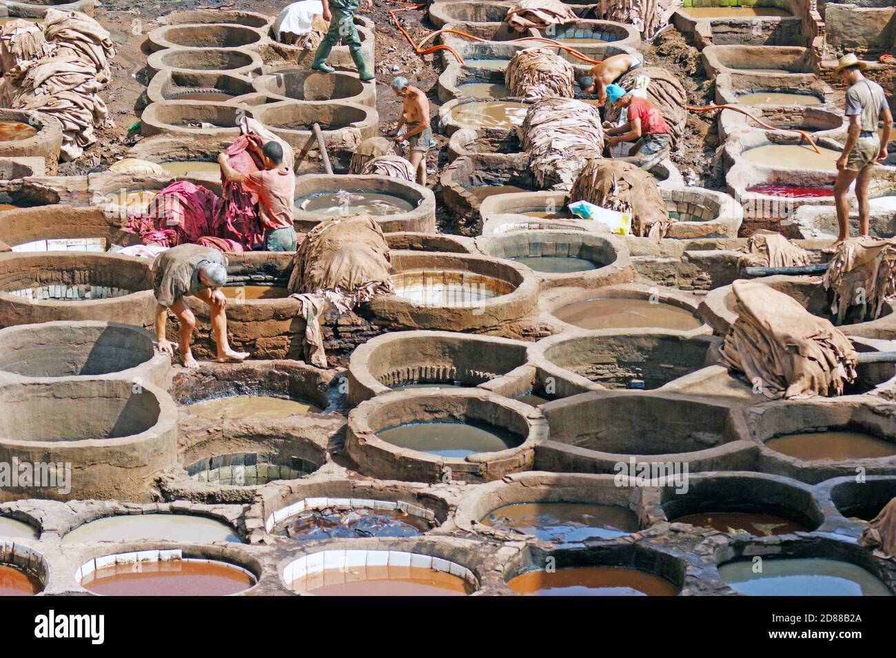 Manual laborers work the stone vats at the Chouara Tannery in Fez, Morocco where hides are softened and dyed for the leather industry. Stock Photo