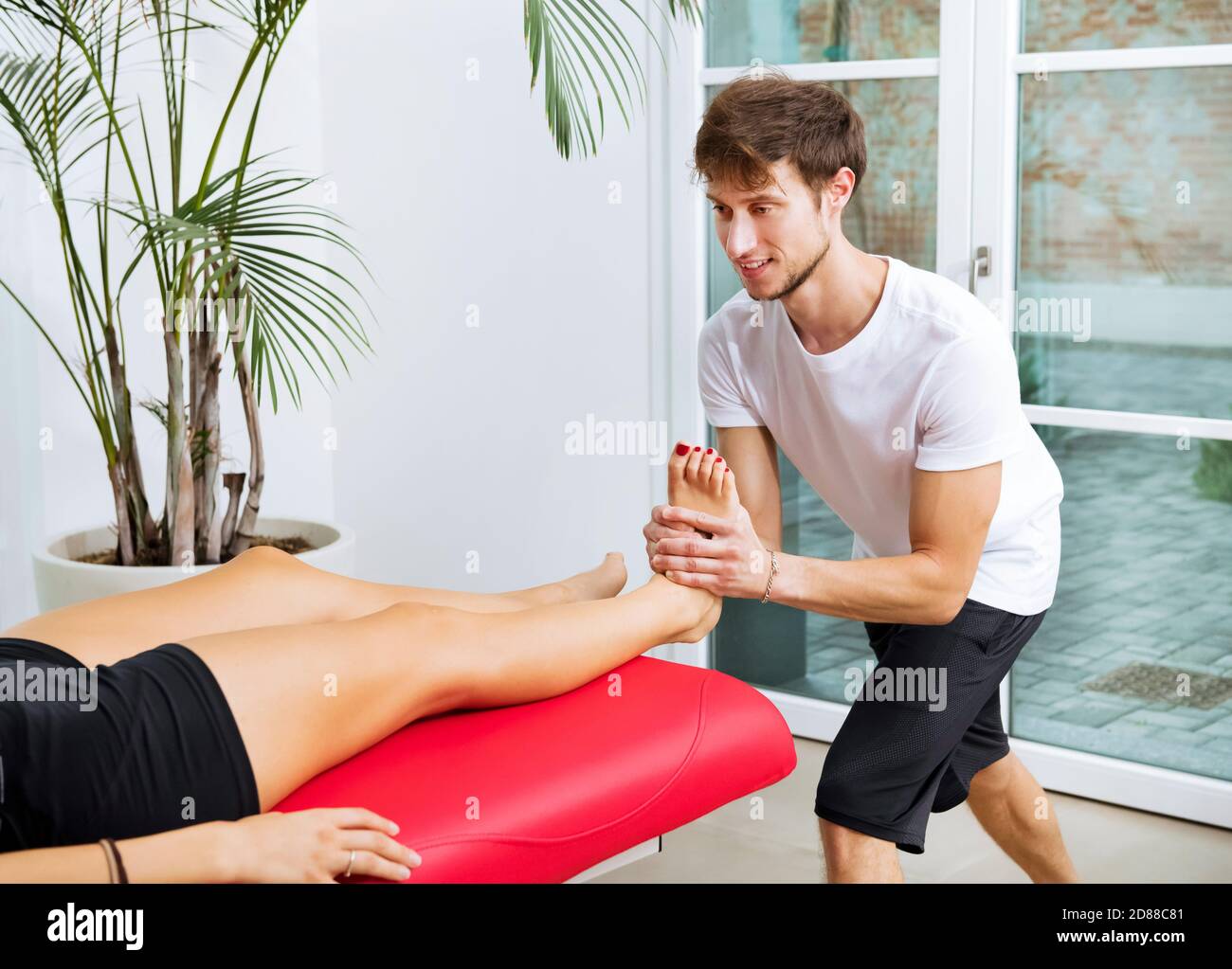 Osteopath doing an ankle decontraction on a young female patient in his clinic manipulating the joint and muscles with his hands Stock Photo