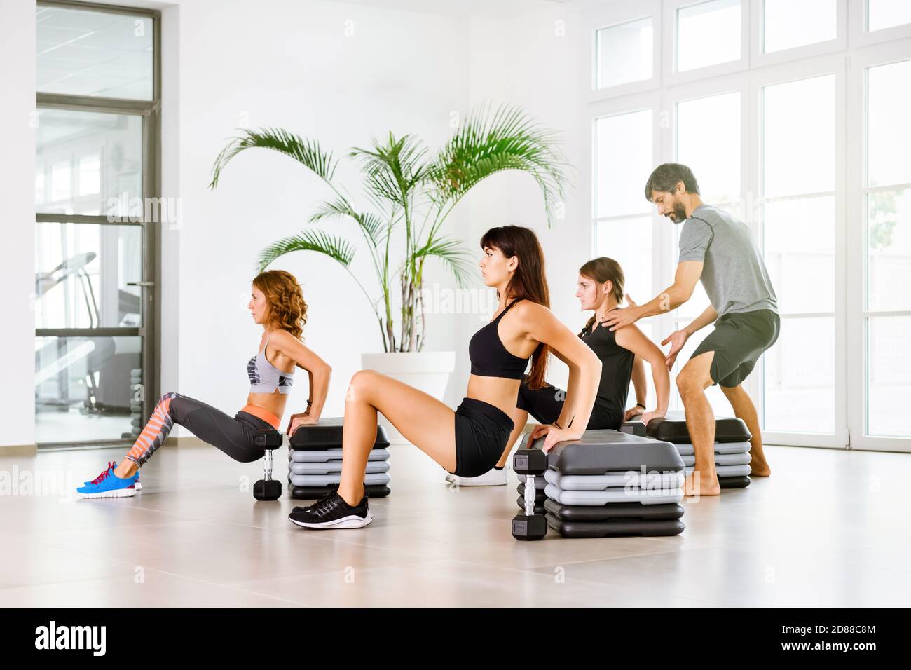 Fitness class with young people doing push down exercise with a personal trainer assisting in a high key gym in a health and fitness or healthy lifest Stock Photo