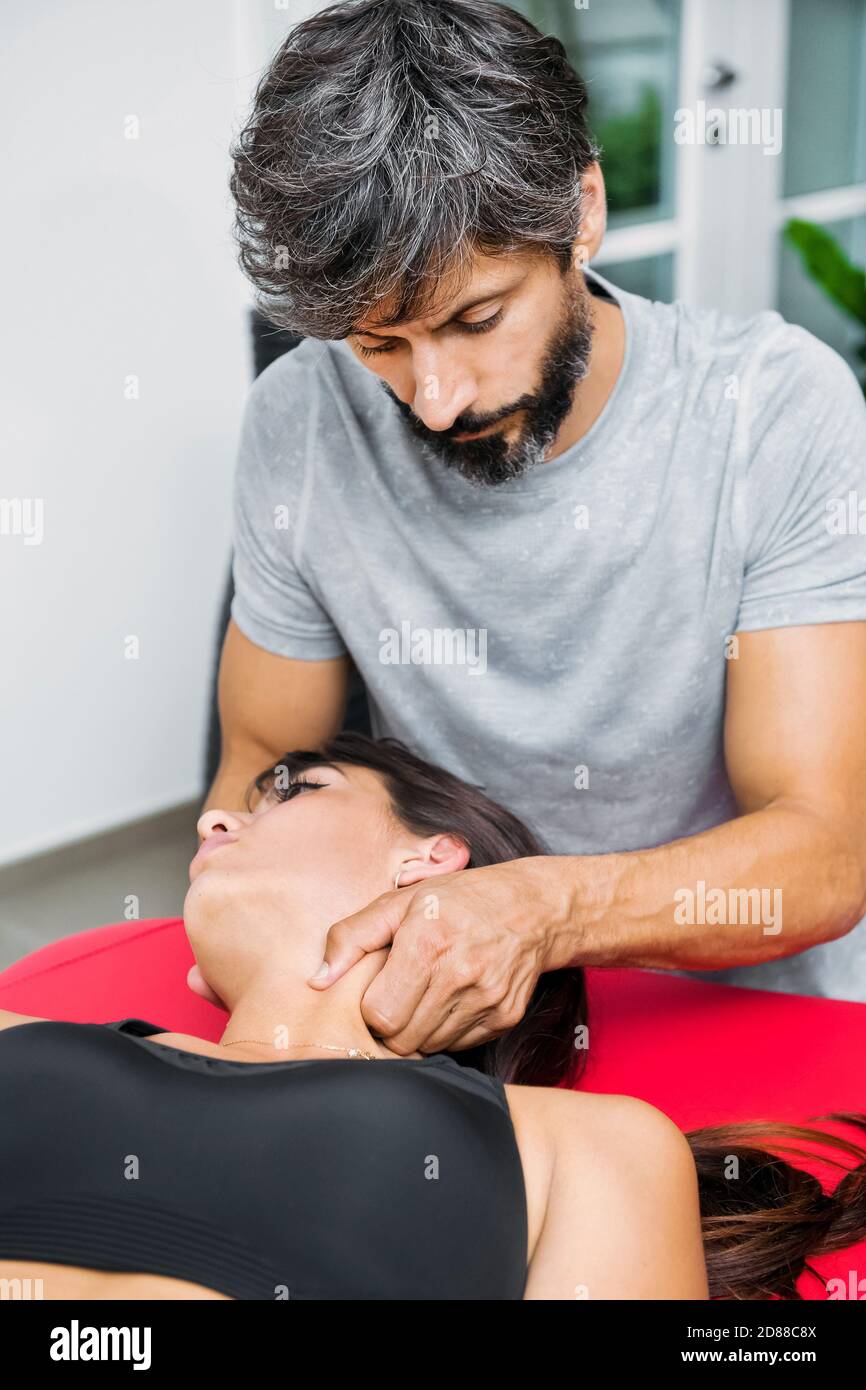 Osteopath performing sternocleidomastoid myofascial massage on a cervical muscle in the neck of a young woman during a treatment in his clinic Stock Photo