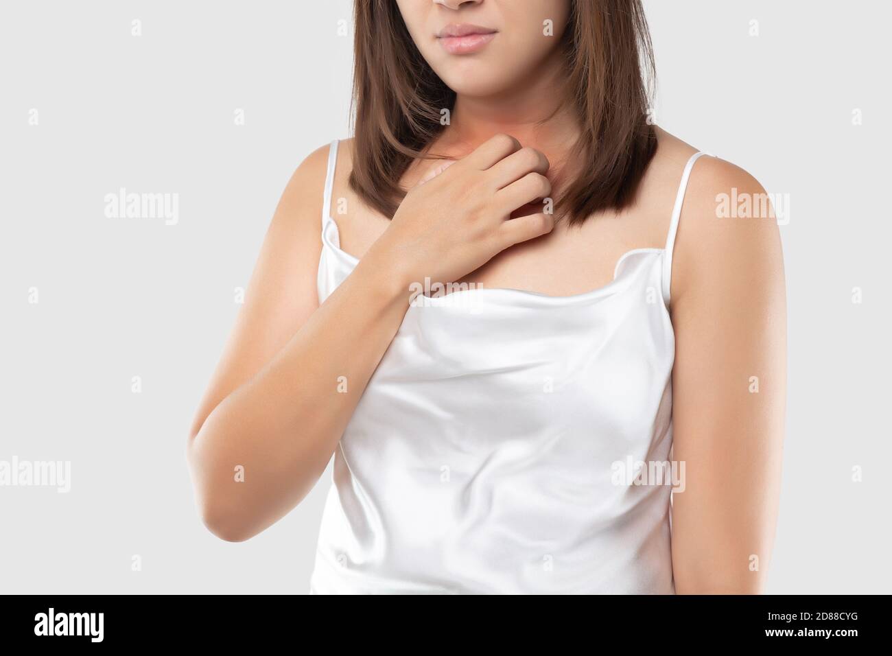 A woman in the white satin dress is scratching their neck due to itching on a gray background. Female with dry skin. The concept of allergy symptoms a Stock Photo