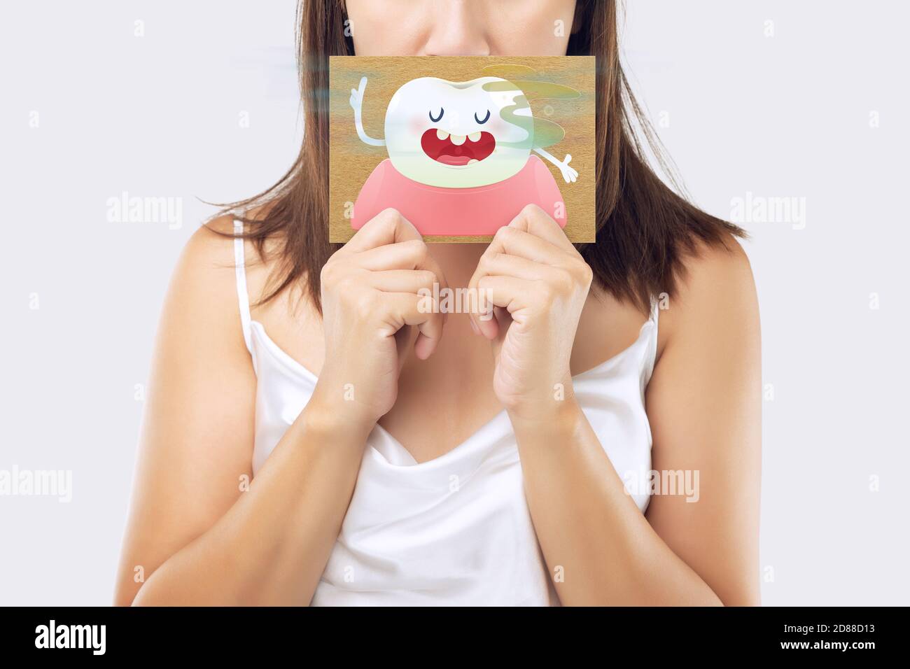 A woman wearing a white dress holding a white paper with an open mouth cartoon image. On a light gray background. Bad breath or Halitosis. The concept Stock Photo