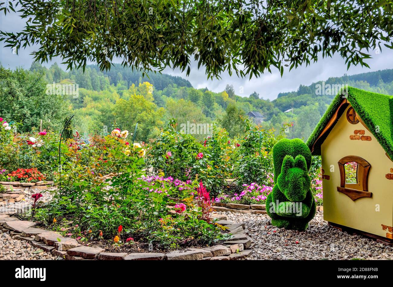 Novokuznetsk, Russia - August 15, 2020: Green sculpture of squirrel near little house, created from artificial grass - gardens topiary. Rose garden - Stock Photo