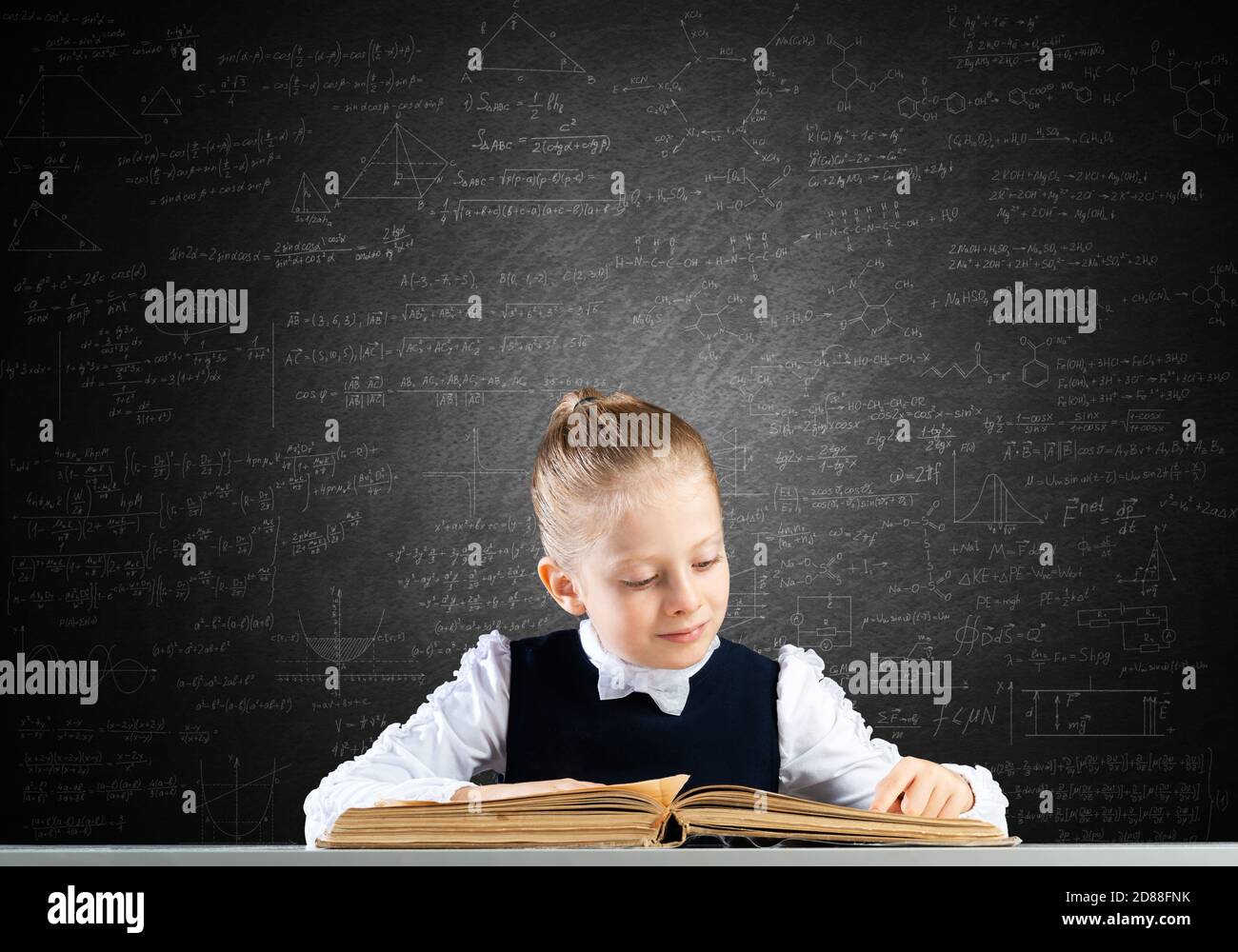 Smiling little girl sitting at desk with open book Stock Photo - Alamy