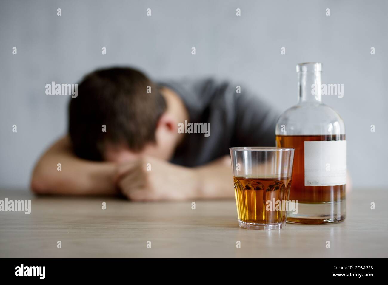 alcoholism and depression concept - close up of glass and bottle of whiskey and drunk man lying on the table Stock Photo