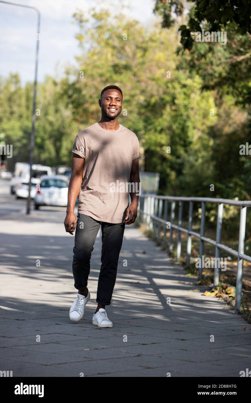Young black man walking on city sidewalk smiling. Full length. Vertical. Stock Photo