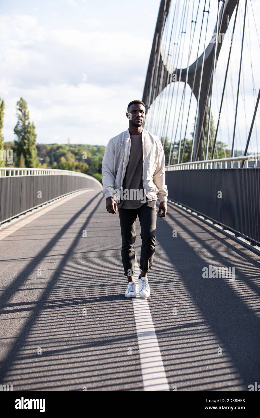Handsome black man walking on pedestrian bridge with confidence. Full length. Vertical. Stock Photo