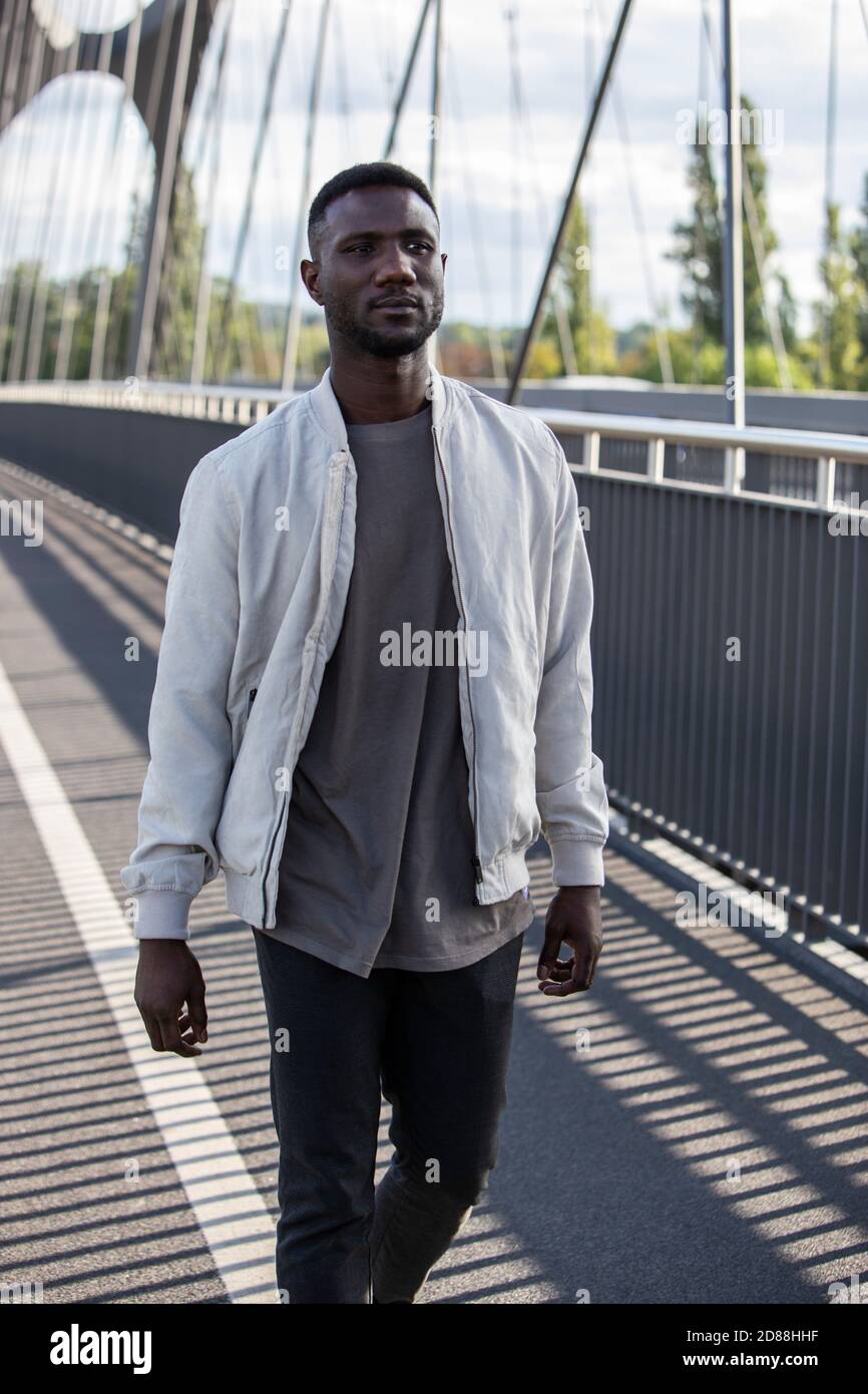 Handsome young black man walking on bridge with confident expression. Three quarter length. Vertical. Stock Photo