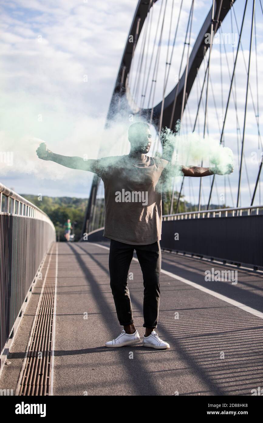 Man holding green colored smoke bombs with arms stretched out. Full length. Vertical. Face Obscured. Stock Photo