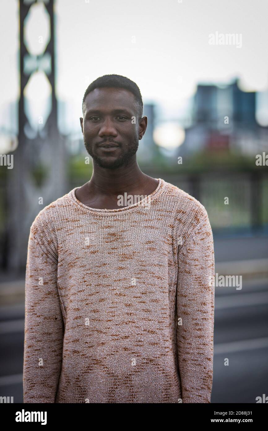 Handsome black man posing in sweater standing outdoors. Medium shot. Focus on foreground. Front view. Stock Photo