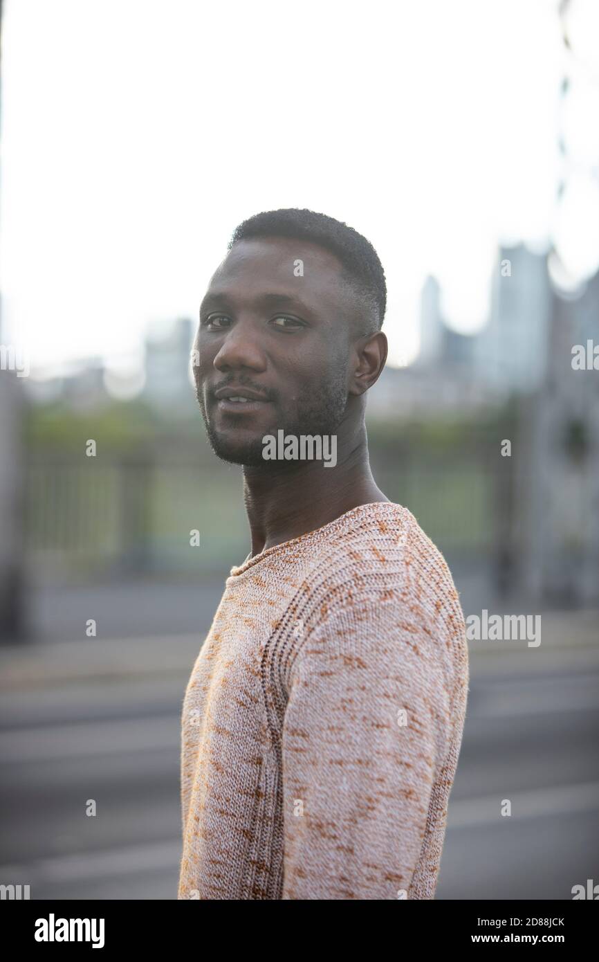 Portrait of handsome man turning head looking at camera. City background. Shallow depth of field. Medium shot. Stock Photo