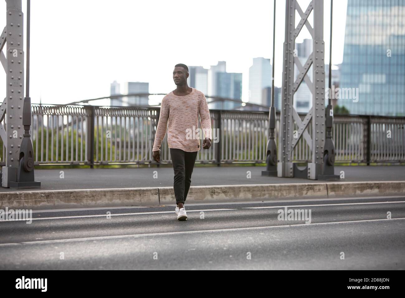 Young black man crossing street with city background. Long shot. Stock Photo