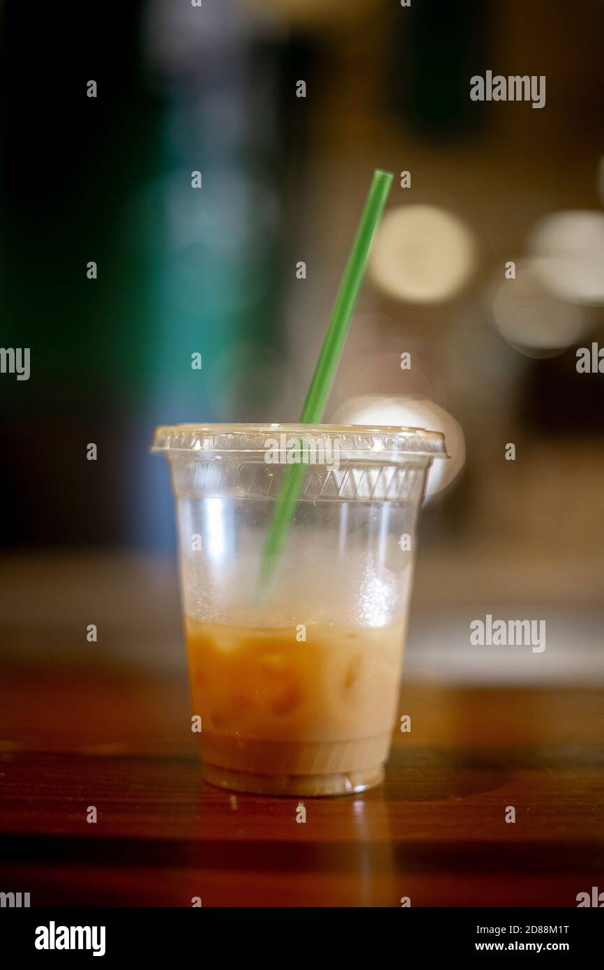 Cold coffee sitting on a wooden table with a green straw and ice inside of a plastic to go cup. Stock Photo