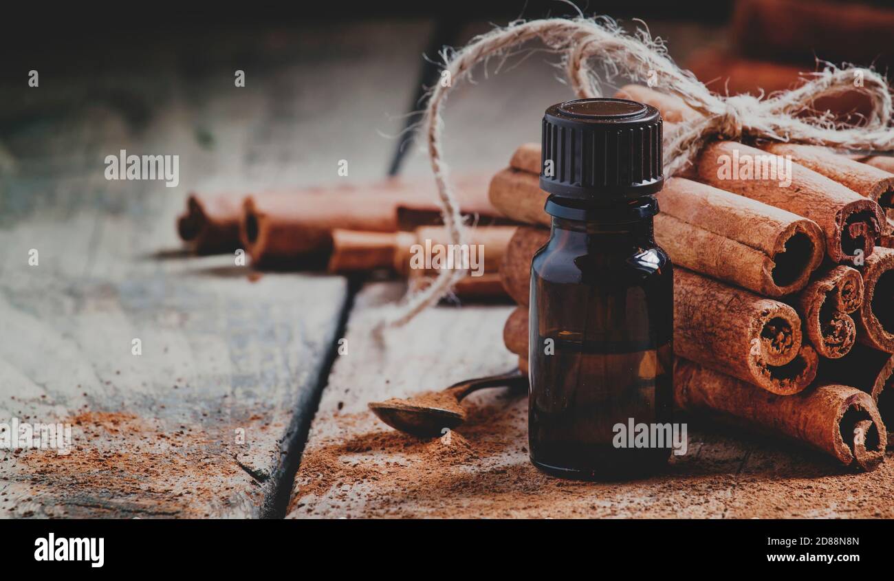 Essential cinnamon oil in a small bottle, ground cinnamon and cinnamon sticks on old wooden background, selective focus  and toned image Stock Photo