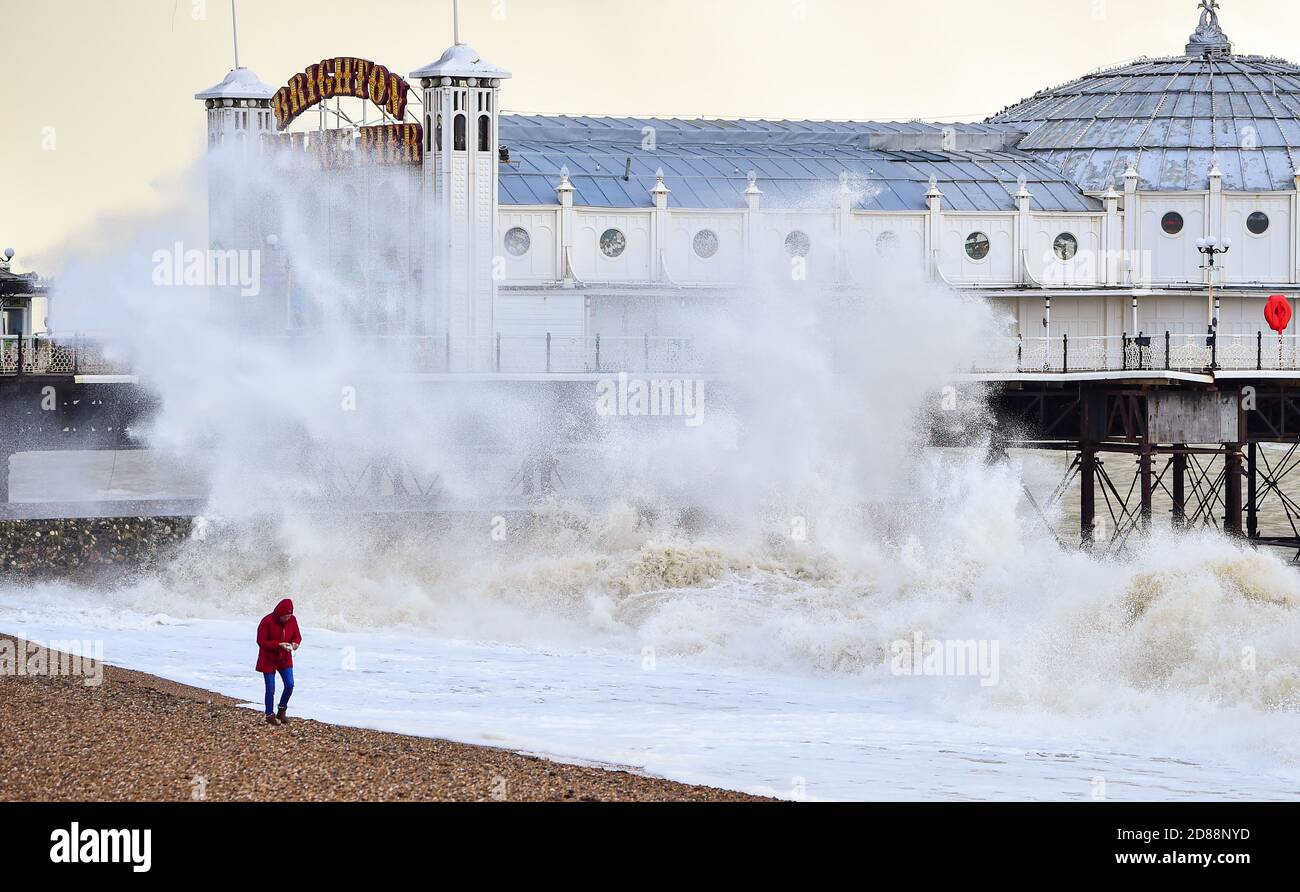 Brighton UK 28th October 2020 - A woman walks on the beach as huge waves crash in by Brighton Palace Pier as stormy weather is forecast for parts of Britain due to the tail end of Hurricane Epsilon  : Credit Simon Dack / Alamy Live News Stock Photo