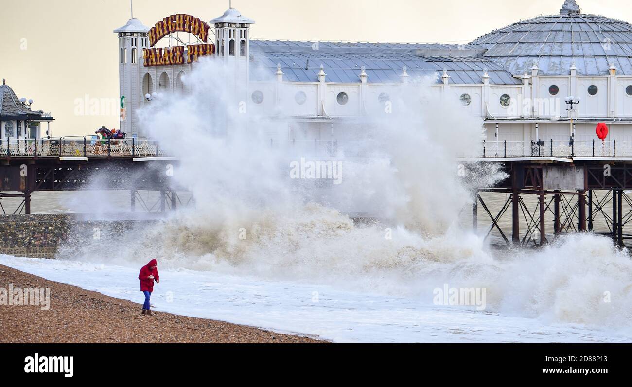 Brighton UK 28th October 2020 - A woman walks on the beach as huge waves crash in by Brighton Palace Pier as stormy weather is forecast for parts of Britain due to the tail end of Hurricane Epsilon  : Credit Simon Dack / Alamy Live News Stock Photo