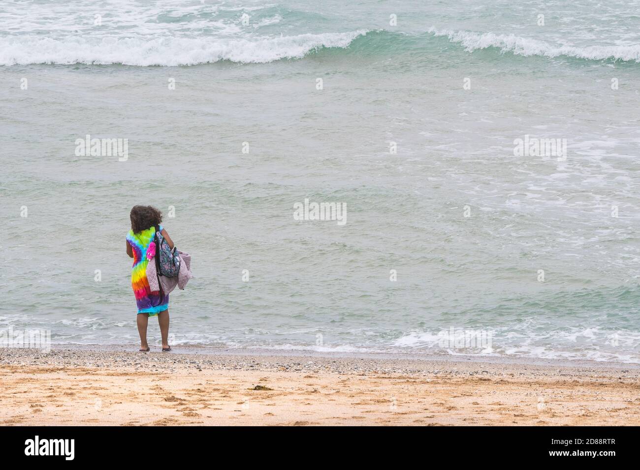 A holidaymaker on a staycation holiday wearing a colourful dress standing on the shore line on Fistral Beach in Newquay in Cornwall. Stock Photo