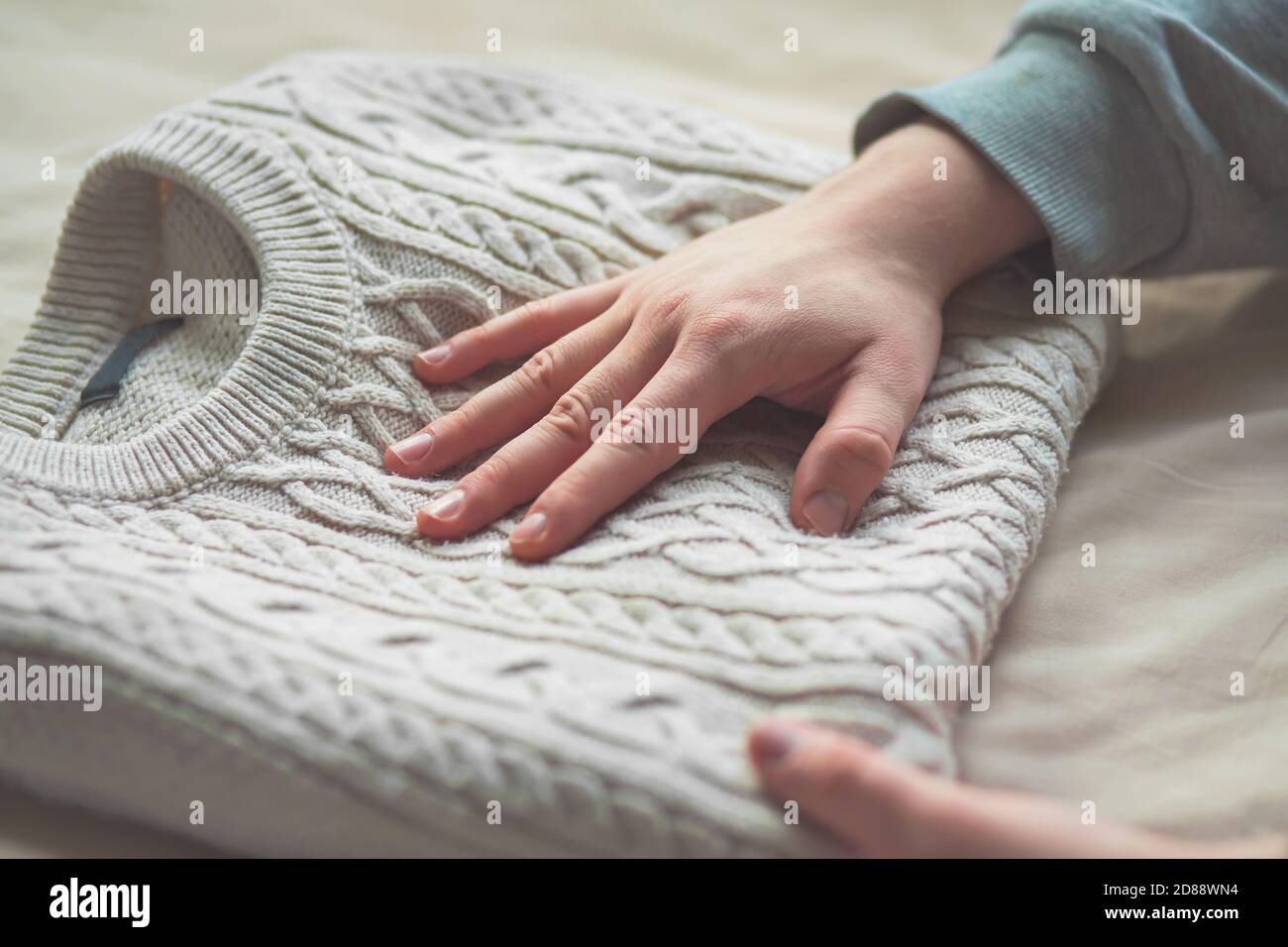 A man in gray clothes puts a soft white warm sweater in a neat pile, and gently strokes his hand over the pleasant fabric. Clothing for cold days. Stock Photo