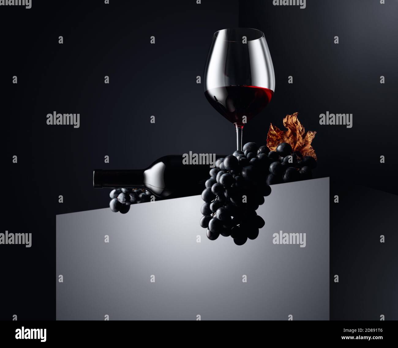 Red wine and blue grapes with dried up vine leaves on a dark background ...