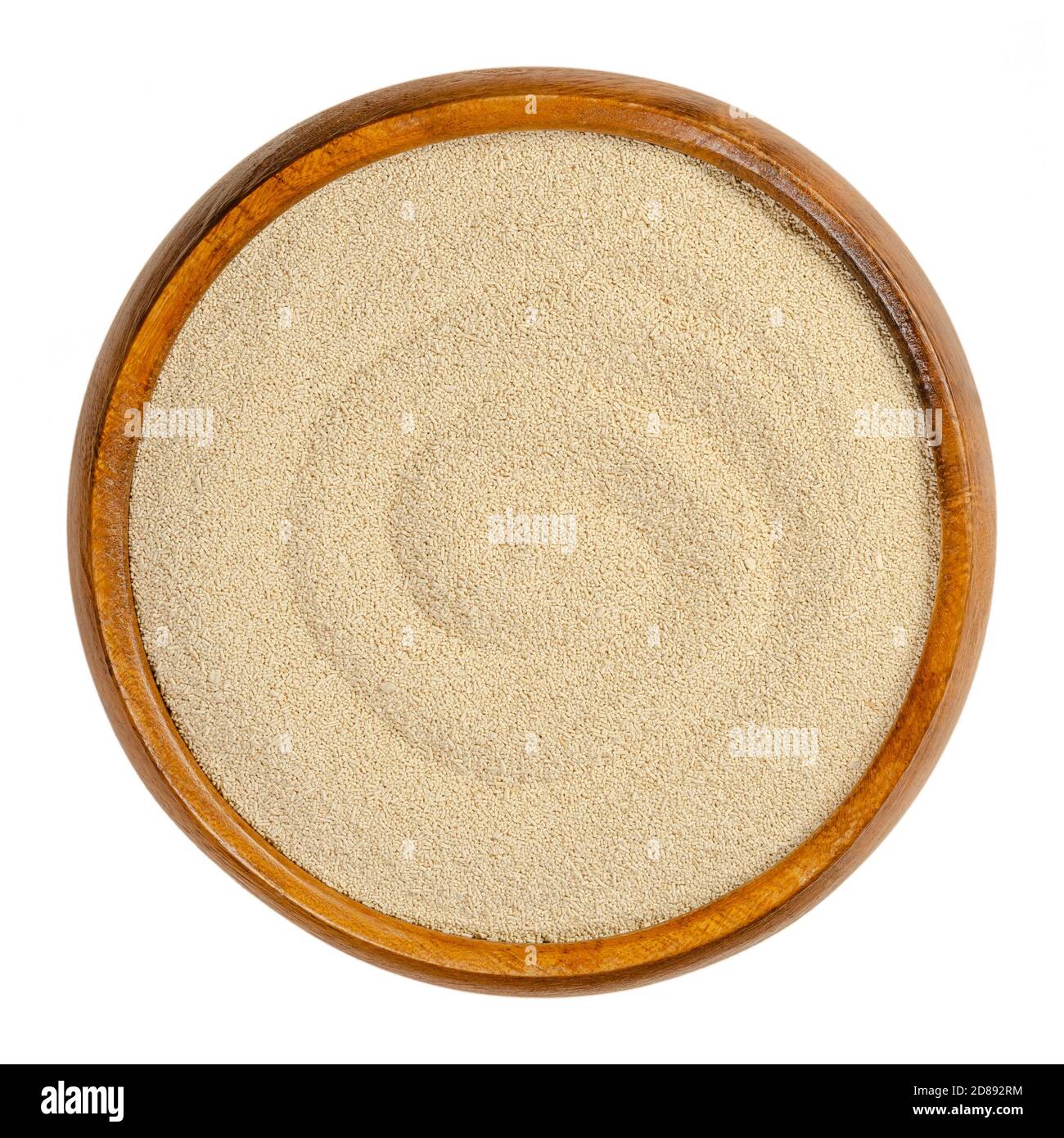 Dry yeast in a wooden bowl. Small oblong granules of active bakers yeast, commonly used in baking bread and bakery products. Close-up, from above. Stock Photo