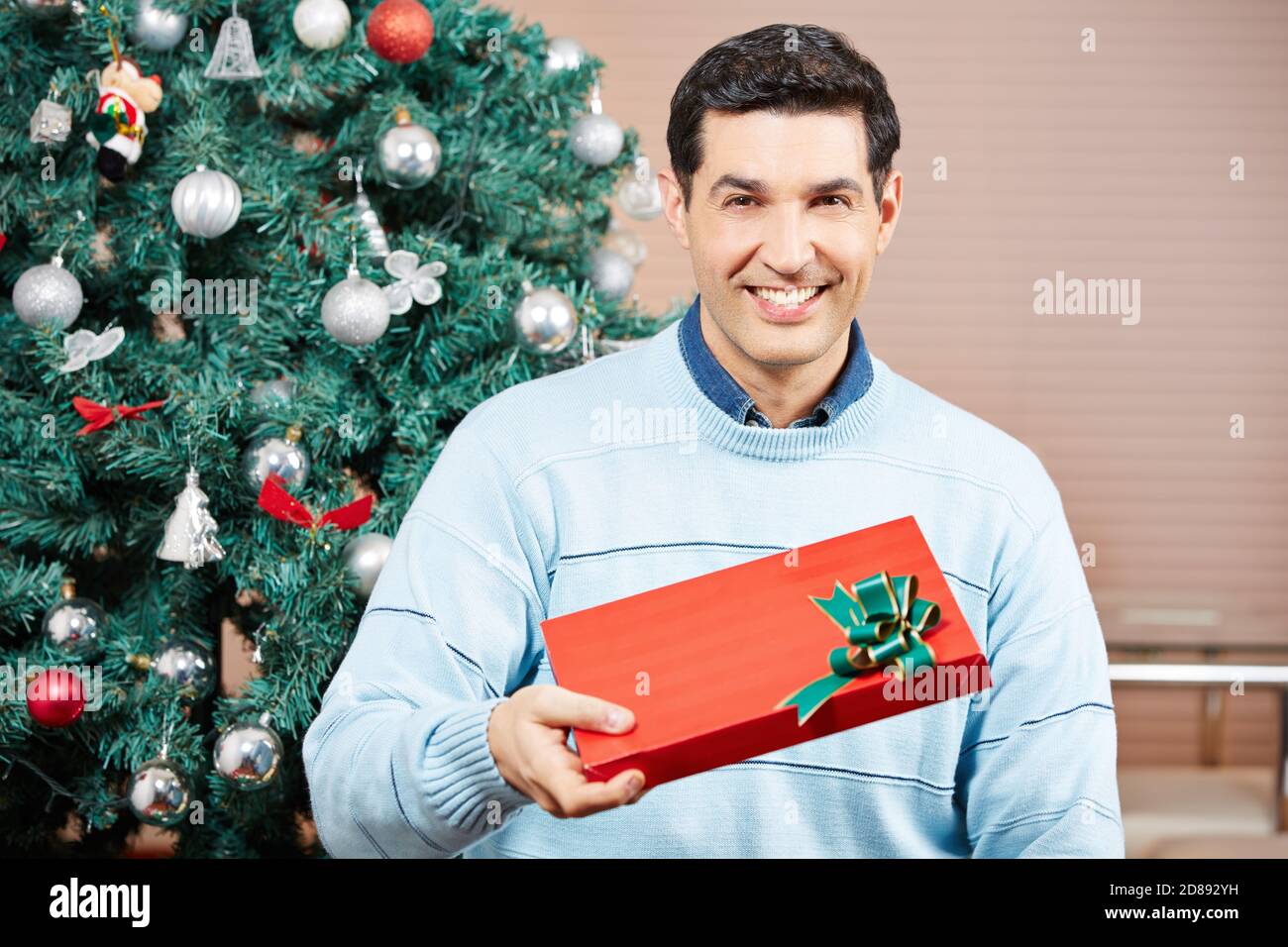 Smiling man with a red Christmas present next to a Christmas tree Stock Photo