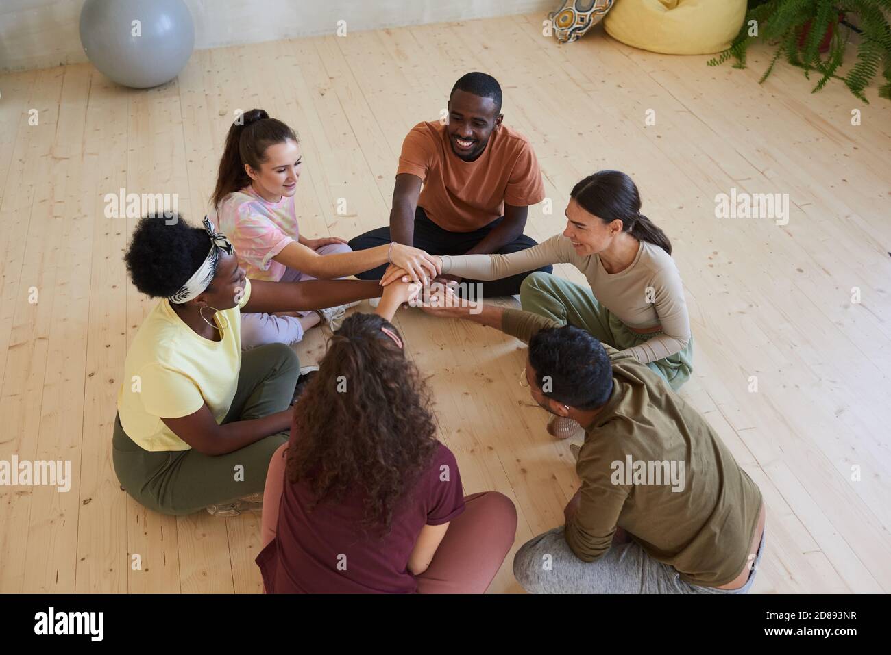 Multiethnic group of people sitting on the floor in circle and holding hands during classes Stock Photo