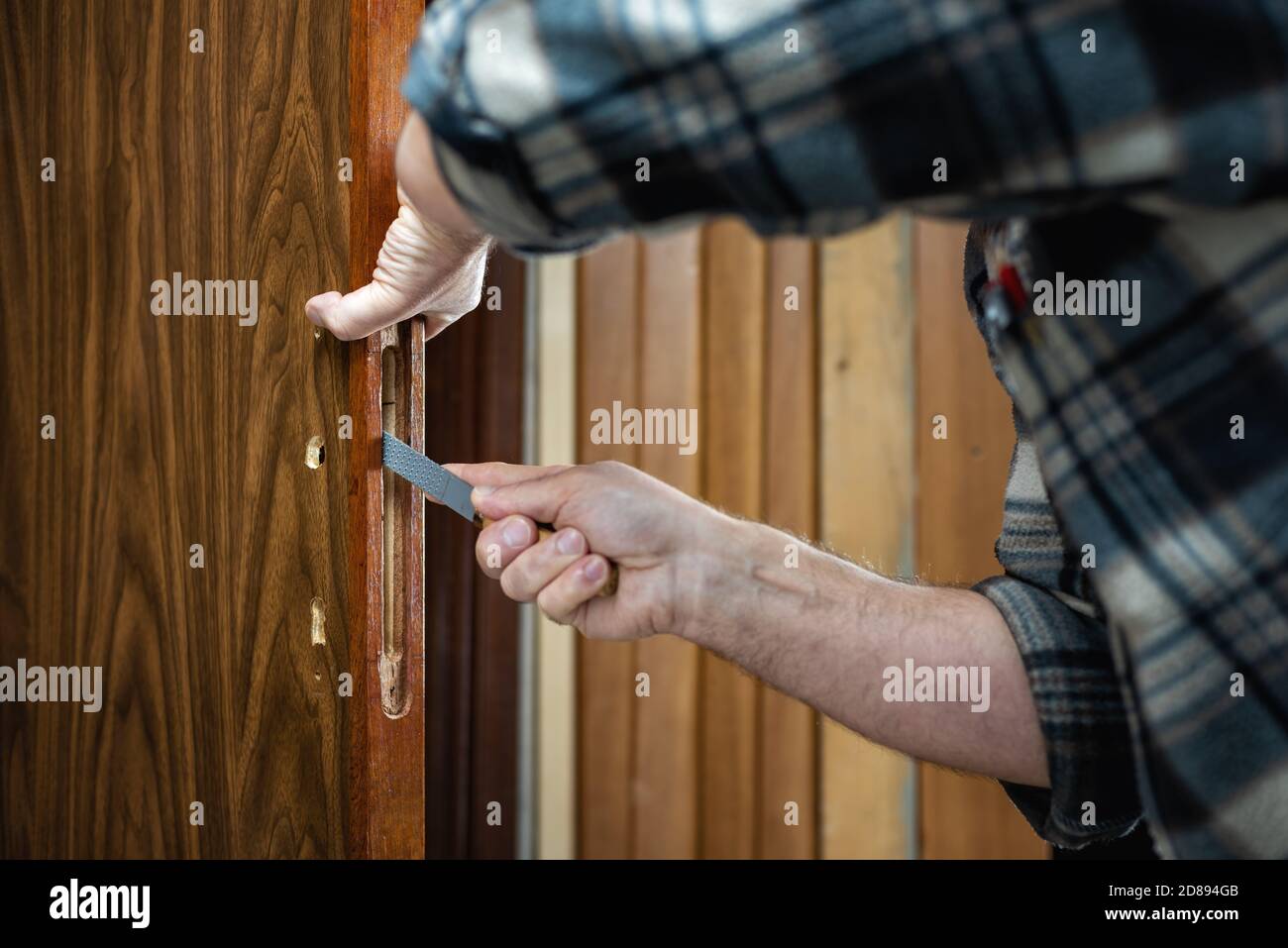Close-up. Carpenter with the rasp prepares the hole for the lock of a wooden door. Construction ...