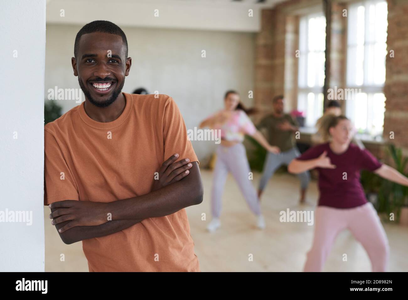 Portrait of African young man working as a dance instructor smiling at camera with people exercising in the background Stock Photo