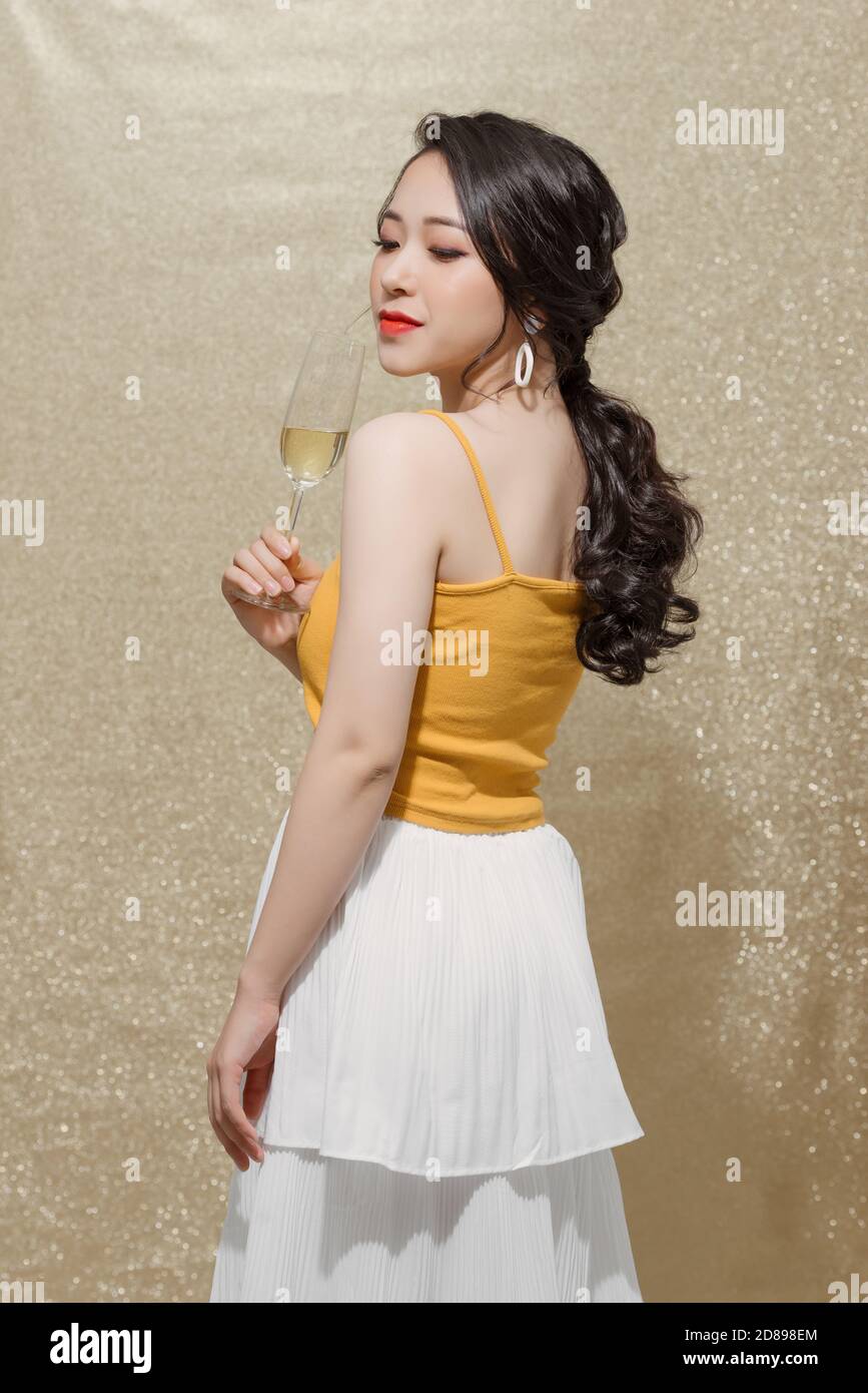 Feminine asian model raising glass of champagne standing over sparkles background Stock Photo